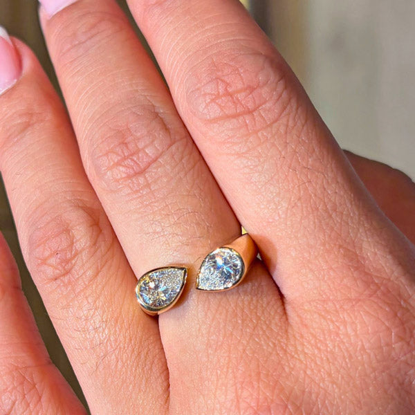 Close-up of a 18K yellow gold open ring featuring two bezel-set pear-shaped diamonds worn on a woman's finger.