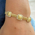 A gold bangle bracelet with three textured square links, each bordered by pave diamonds, shown worn on a wrist.